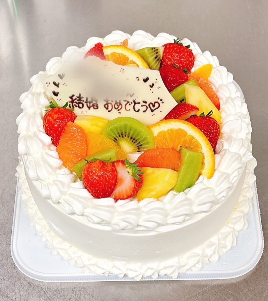 結婚おめでとうのチョコプレートとフルーツをのせた白い丸いオーダーケーキ