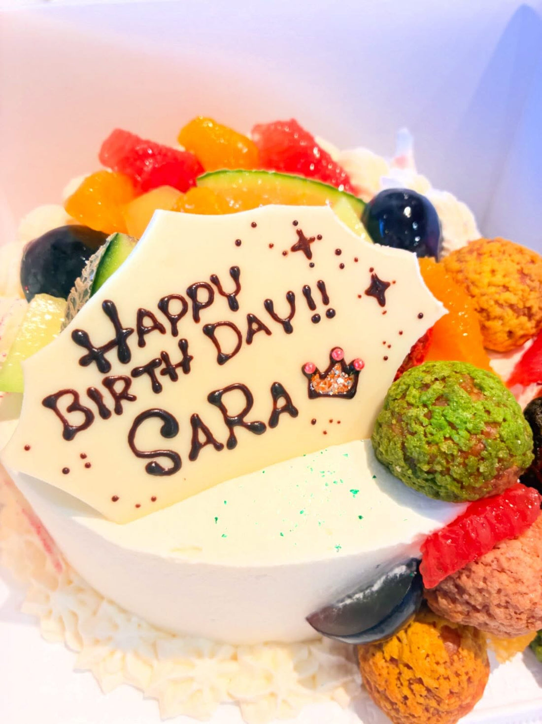 フルーツとカラフルなシューをのせた「HAPPY BIRTH DAY!! SARA」のお誕生日ケーキ