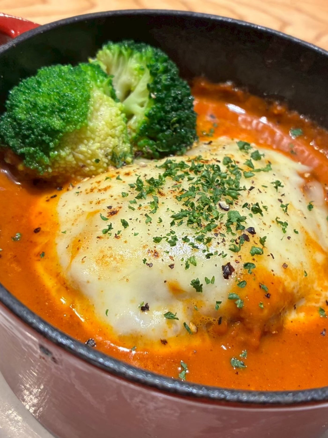 赤い鍋に入った、チーズをのせた鶏ハンバーグとオレンジ色のカカオカレーソース、ブロッコリー