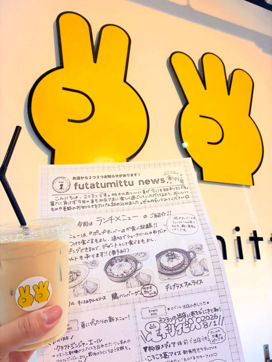 2つ3つのロゴの前で持つ、創刊号の新聞とアイスラテのカップ