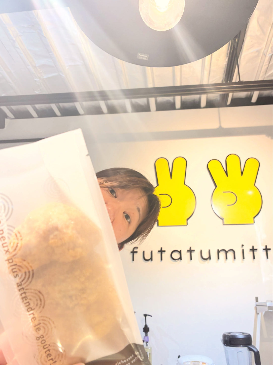 2つ3つの店内で、パイシュー入りの袋を持つスタッフと黄色いロゴの壁