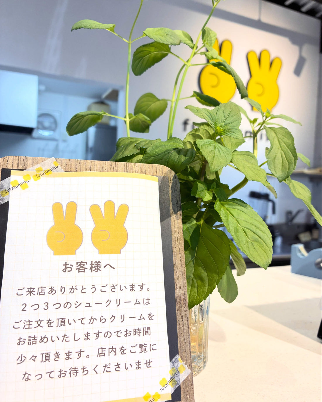 2つ3つの店内カウンターに置かれた、注文後にクリームを詰める旨の案内カードと緑の植物