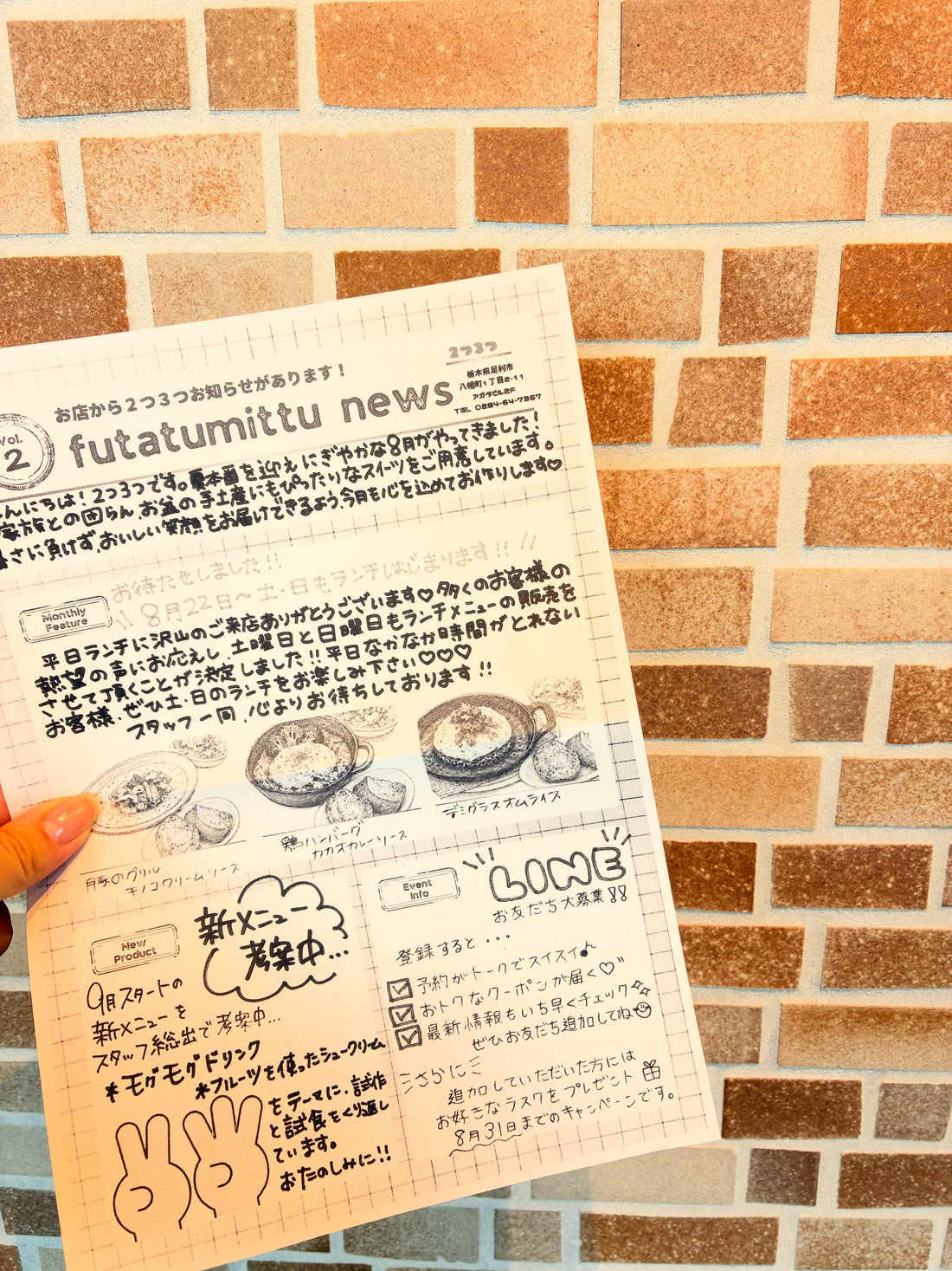 レンガ壁の前で手に持った、2つ3つ新聞No.2のチラシ