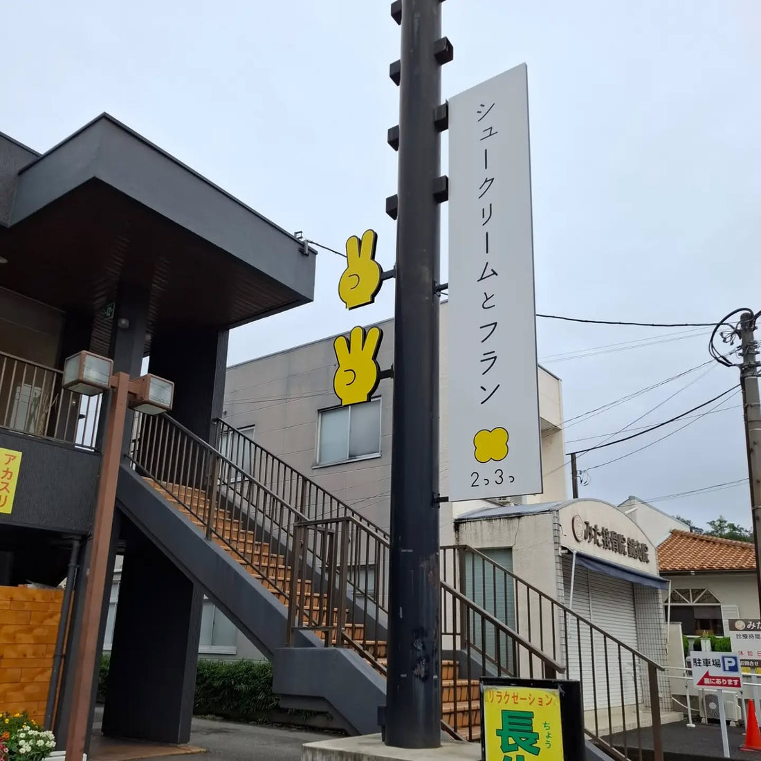 アガタビル前に立つ「シュークリームとフラン 2っ3っ」の白い縦長看板と黄色い指のオブジェ
