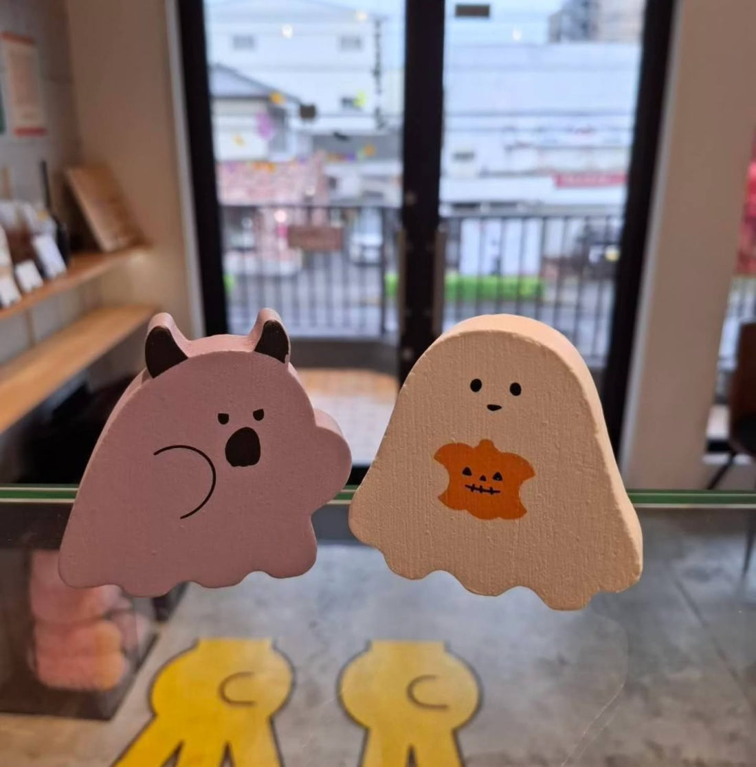 ショーケースの上に並ぶ、角のある薄紫とかぼちゃ柄のクリーム色のハロウィンおばけの木製飾り