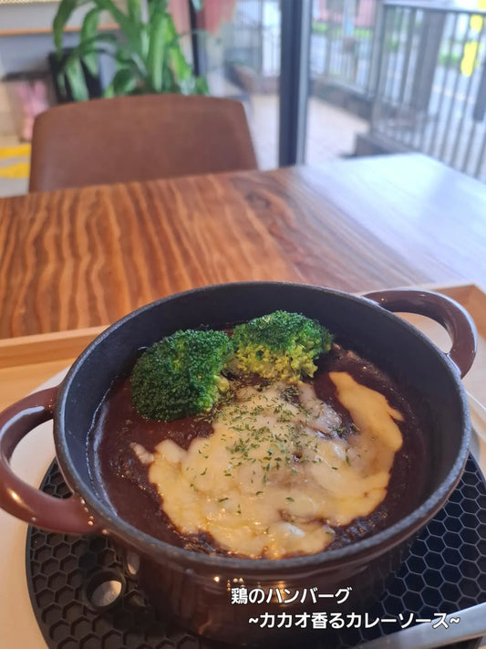 茶色の鍋に入ったチーズのせ鶏のハンバーグ、カカオ香るカレーソース