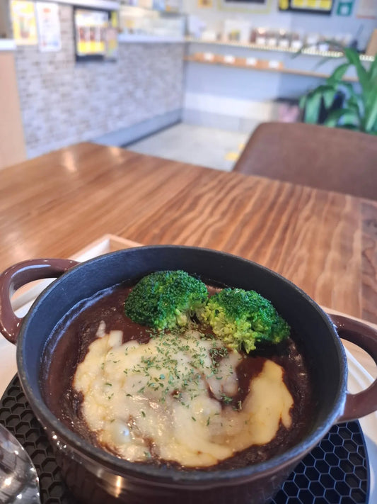 茶色の小鍋に入ったチーズとブロッコリーをのせたカレーソースのハンバーグ