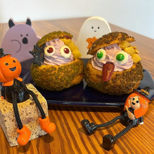 目玉の飾りをのせた紫芋のハロウィンパフェシュー2つと、カボチャ頭の人形やゴーストの飾り