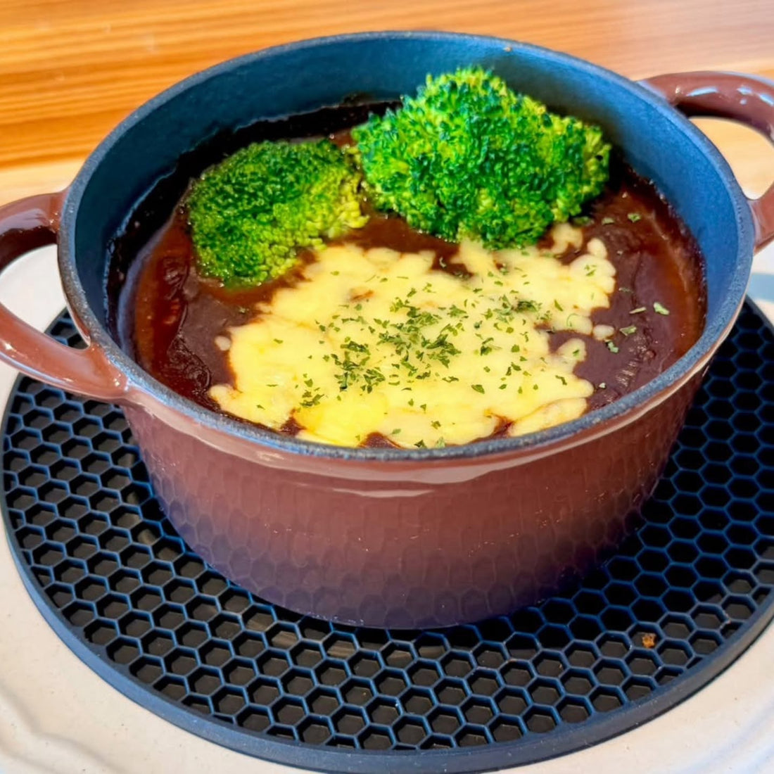 ブロッコリーととろけたチーズがのった、カカオ香るカレーソースのハンバーグ。茶色の鋳物鍋で提供